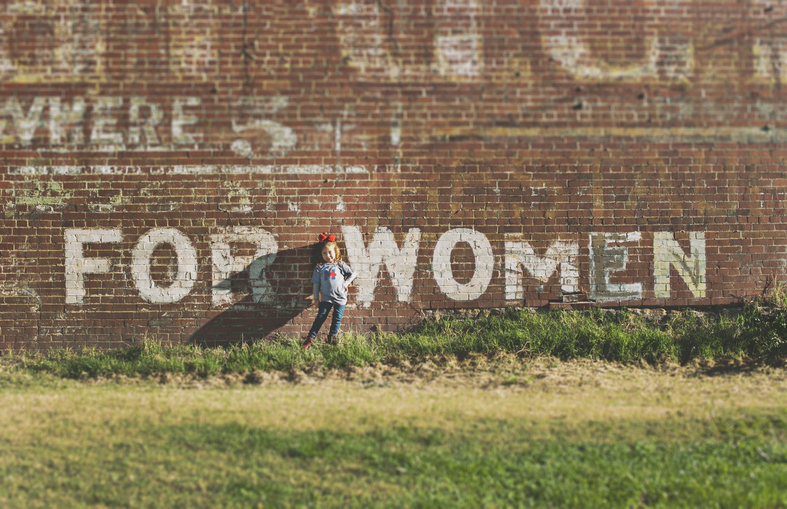 A girl standing in front of a brick wall painted with 'For Women.'