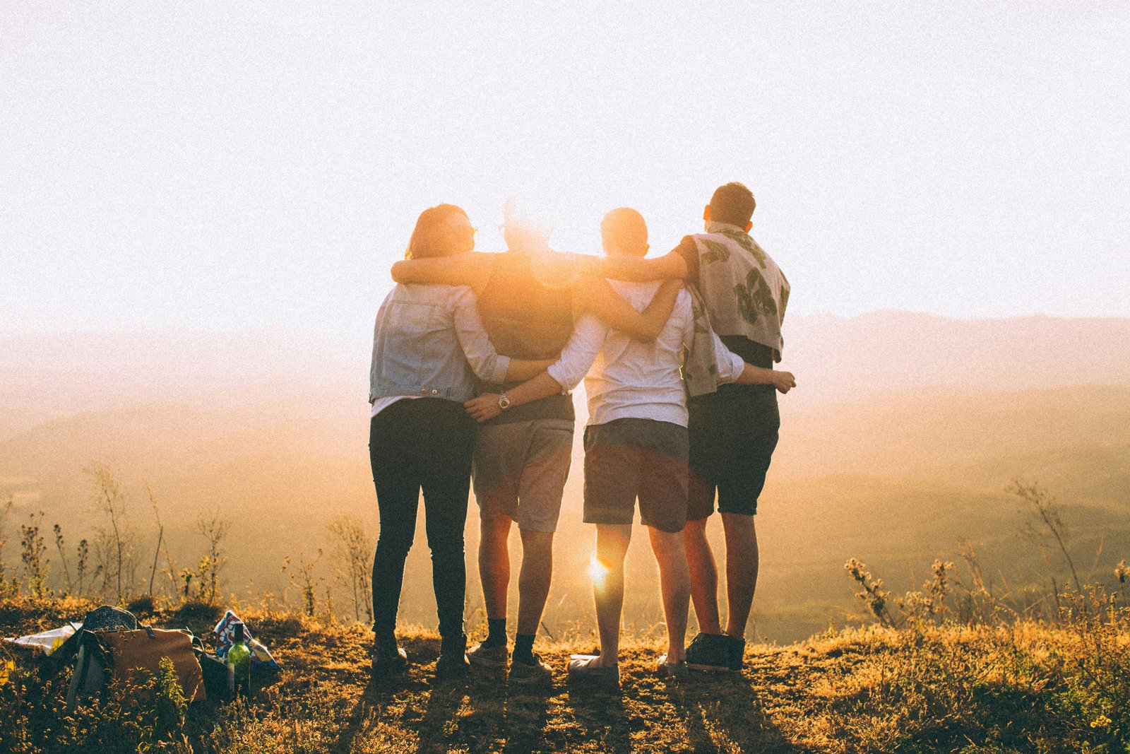 A group of friends stand arm in arm watching the sunset over the hills.