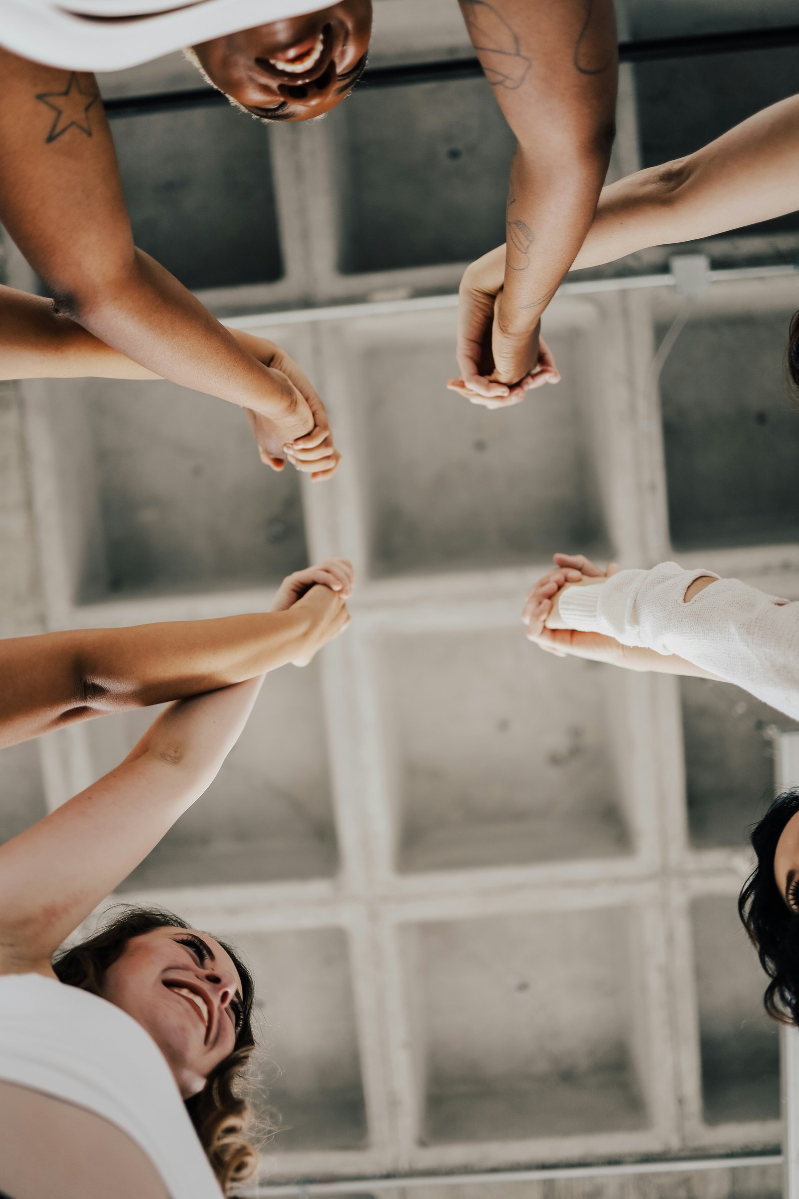 A group of women joining hands together in a circle, viewed from above.