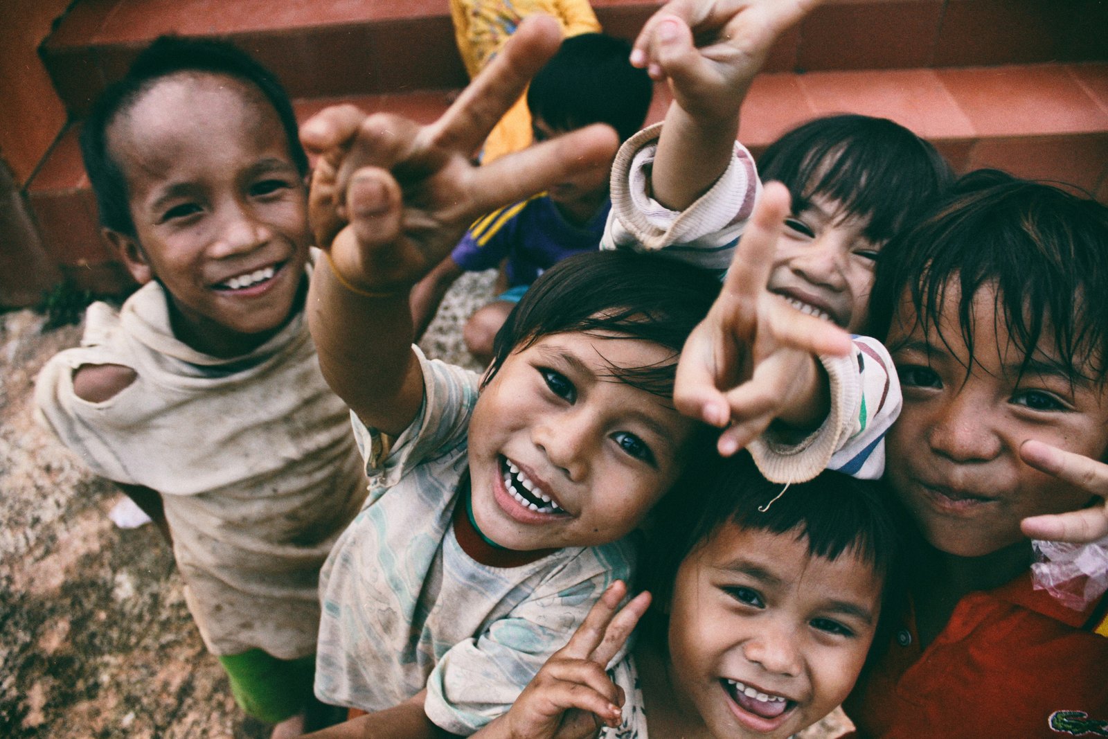 A group of joyful children making peace signs at the camera.