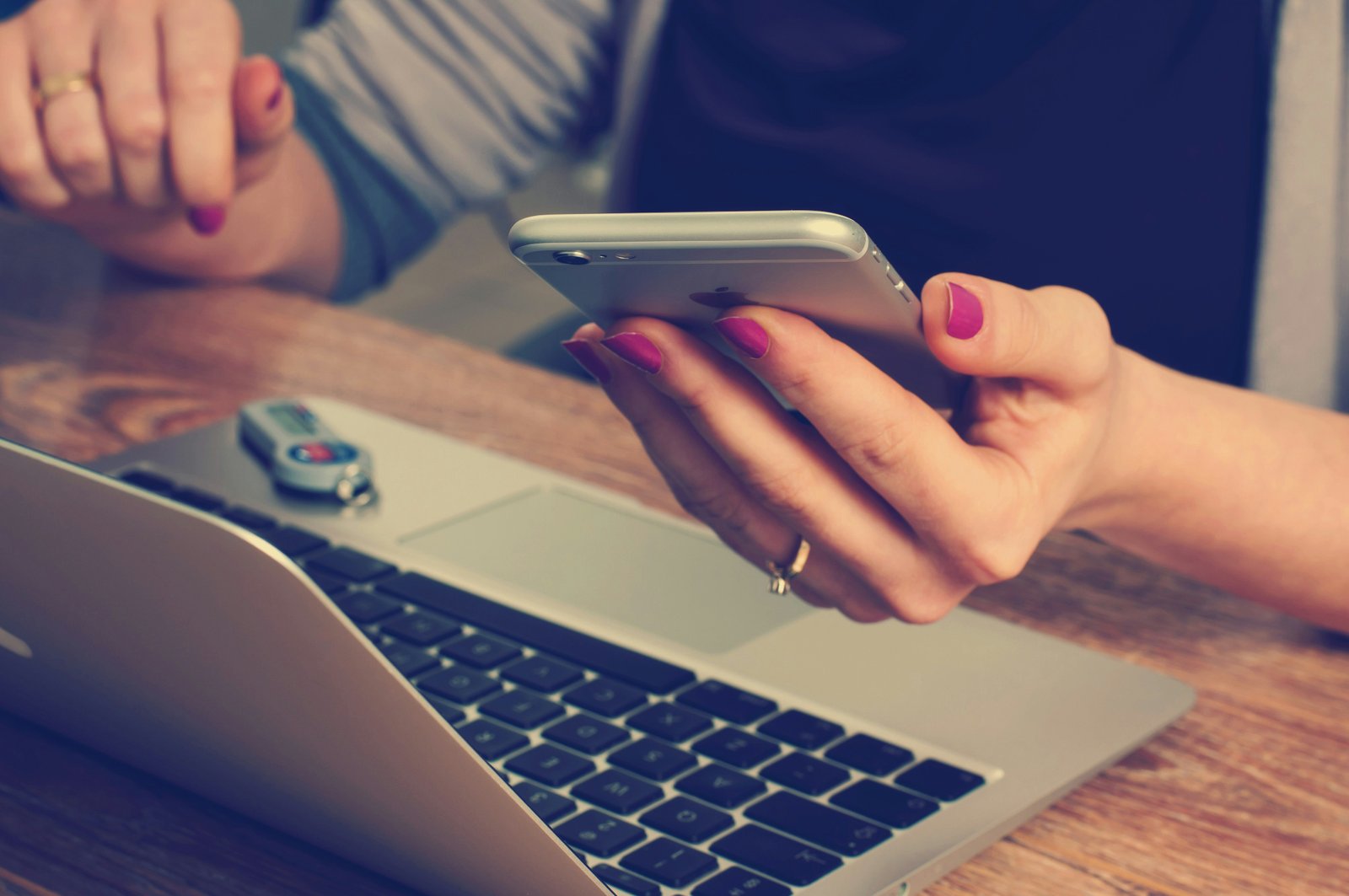 A hand holding a phone beside an open laptop.