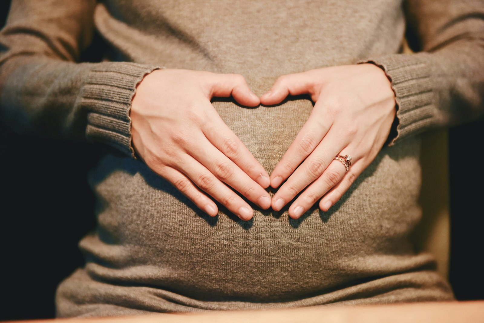 Hands forming a heart shape over a pregnant belly.