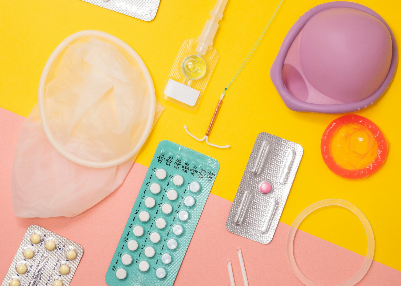A flat lay of reproductive health supplies including contraceptives and an IUD.