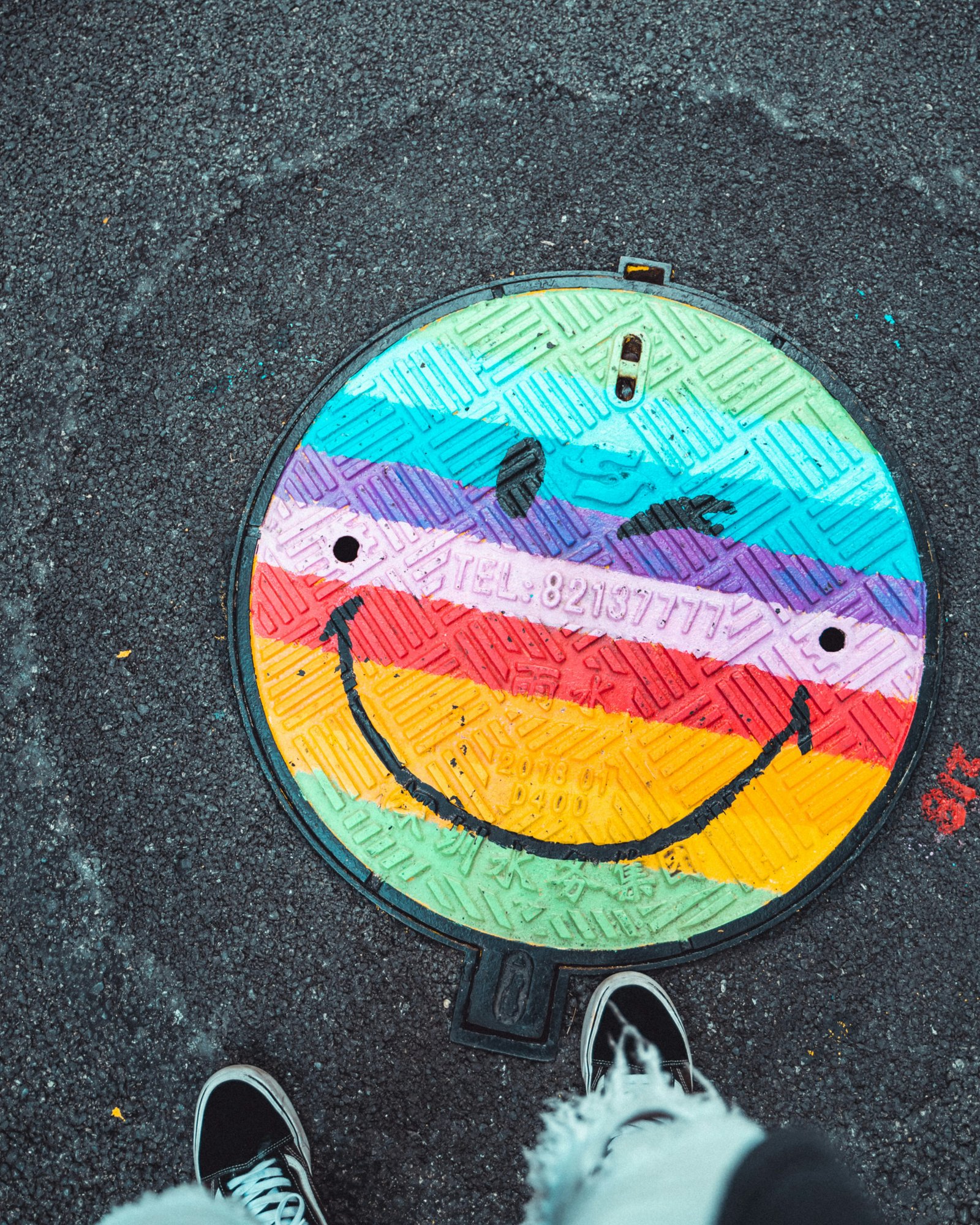 A colorful manhole cover painted like a smiley face on a city street.