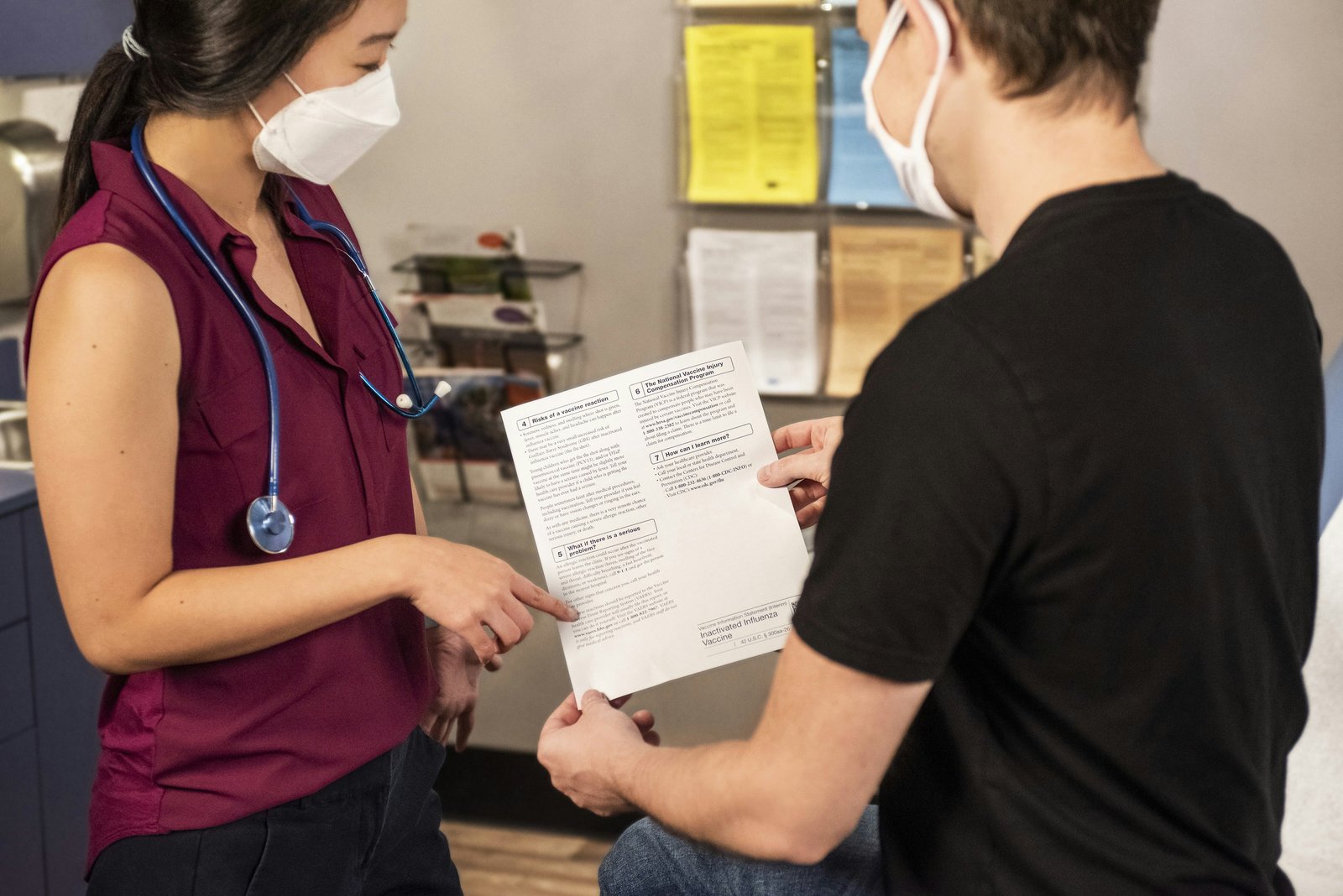 A nurse pointing to a vaccine information sheet while explaining it to a patient.