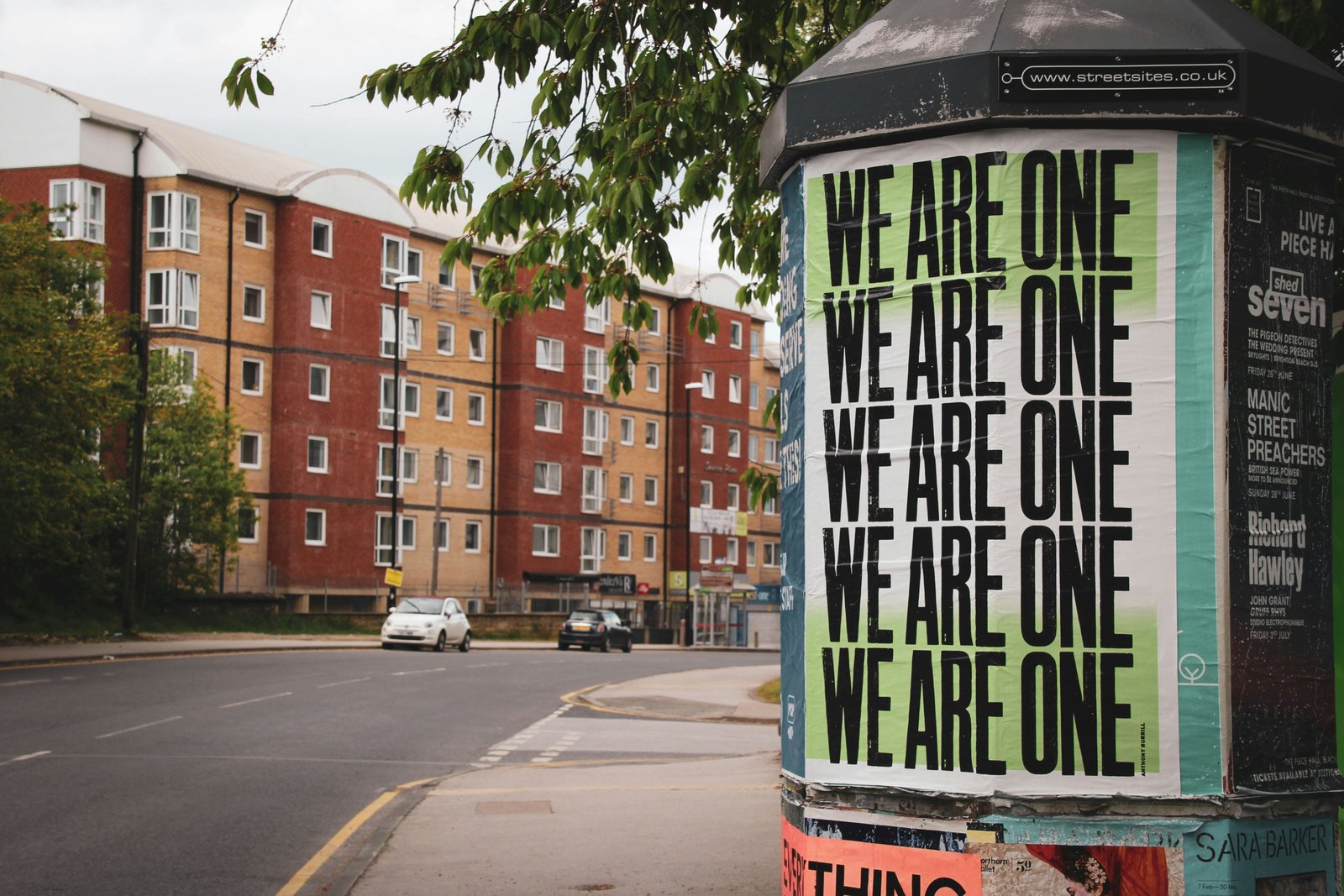 A street poster reading 'We Are One' repeated across the page.